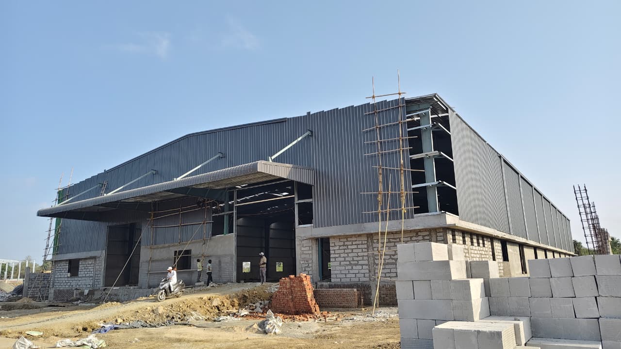 high-performance industrial shed design - bridging the gap between structural integrity and modern aesthetics. modern industrial PEB structure with large cantilevered canopy and insulated metal wall cladding, designed to IS/ AISC standards for heavy-duty storage.
